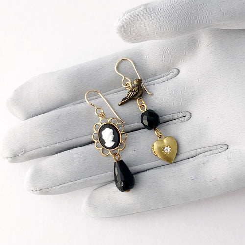 asymmetrical earrings with cameo, black Onyx drop, a dove and tiny heart shaped locket on a gloved hand