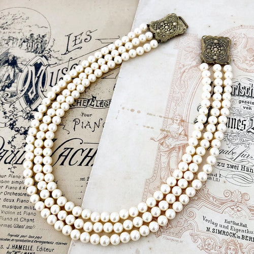 three stranded pearl necklace with buckle clasp lying on vintage music booklets
