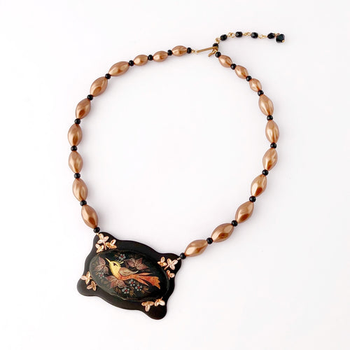 necklace featuring a copper coloured  bird on a black and copper coloured frame with matching beads