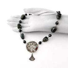 Load image into Gallery viewer, necklace in silvery greys with a red rhinestone set focal displayed on a gloved hand
