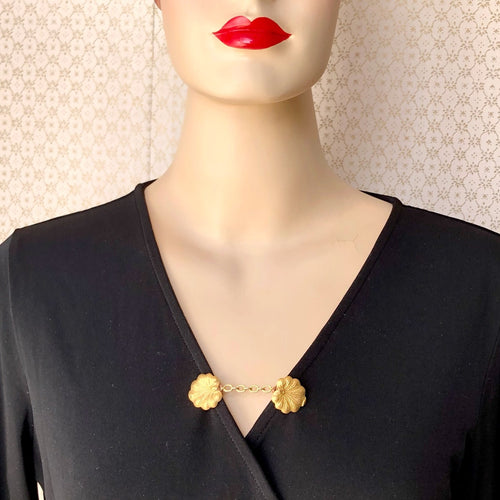 mannequin in a black wrap dress with a sweater clip of lily pads holding the front closed