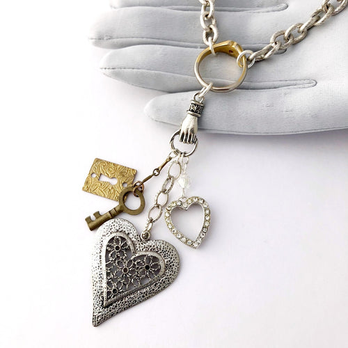 close up of necklace with two hearts, a key and lick charm hanging from a hand shaped connector