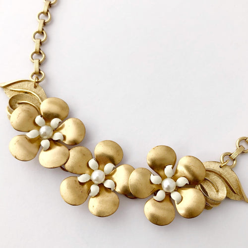 close up of necklace made with vintage brass and white flowers displayed on a white background