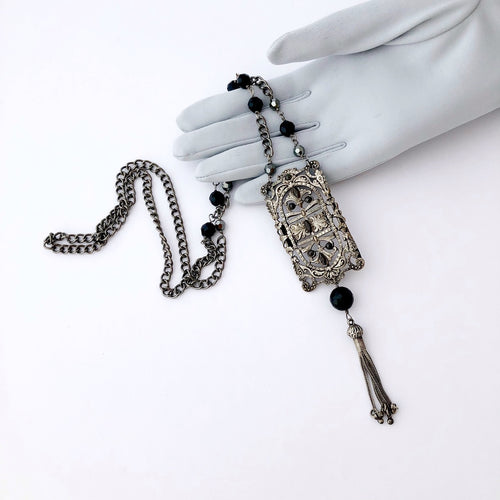 necklace made with a half buckle, chain and beads in silver, grey and black displayed on a gloved hand