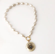 Load image into Gallery viewer, a pearl bead necklace with vintage locket suspended from the front lying flat on a white background

