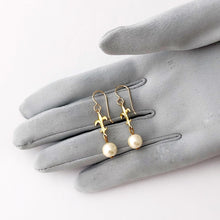 Load image into Gallery viewer, earrings made with pearl beads and fleur-de-lys displayed on a gloved hand
