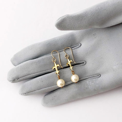 earrings made with pearl beads and fleur-de-lys displayed on a gloved hand