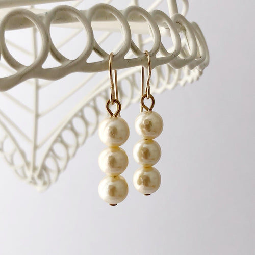 earrings made with three creamy pearl beads hanging from a white frame