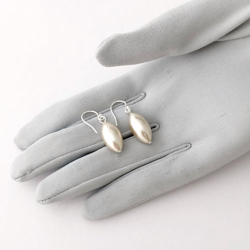 earrings made with silvery white rice shaped vintage pearl beads  displayed on a gloved hand