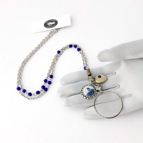 necklace with glass lens, locket and Dutch windmill image, cobalt blue beads and silver chain displayed on a gloved hand
