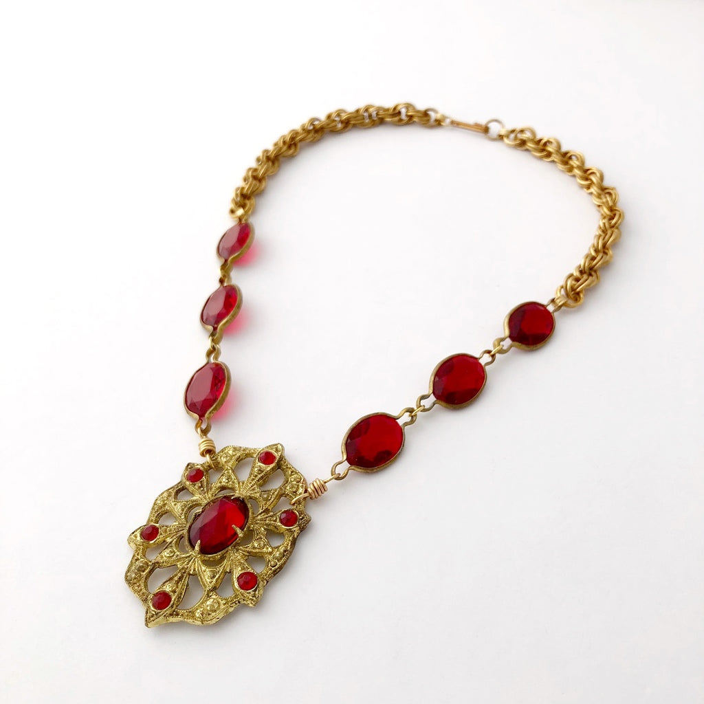 red and gold coloured necklace in medieval style lying flat on a white background